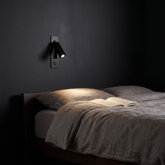 Lumo sconce lighting a book beside a linen bed at night