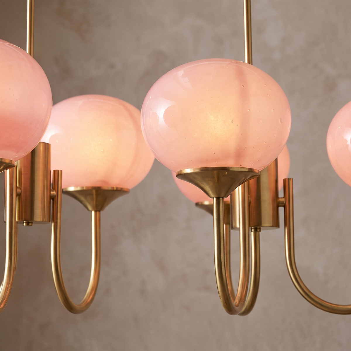 Close detail of the brass arms and blush glass globes of the Bianca chandelier
